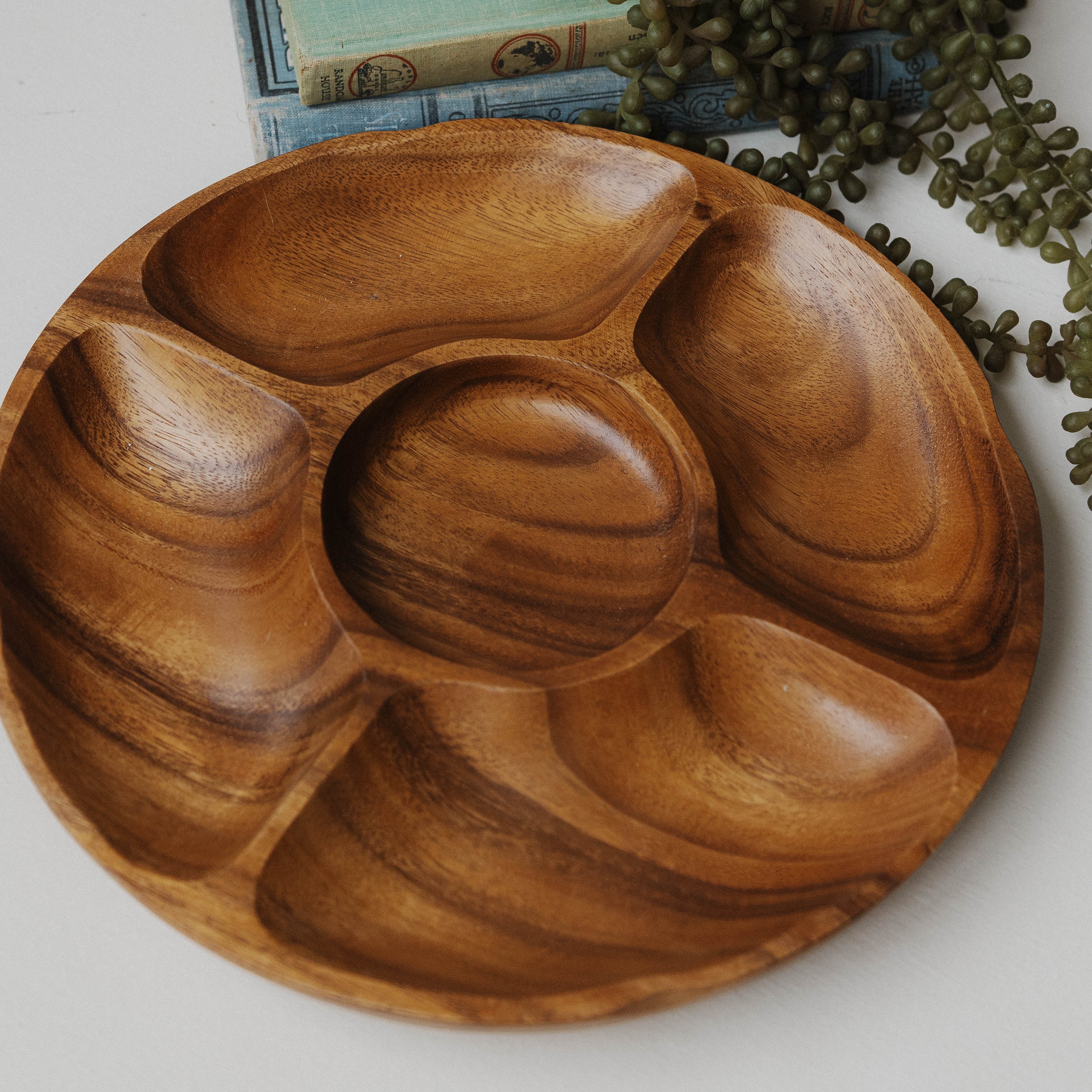 Wooden tray with compartments on a white surface with a plant and books in the background